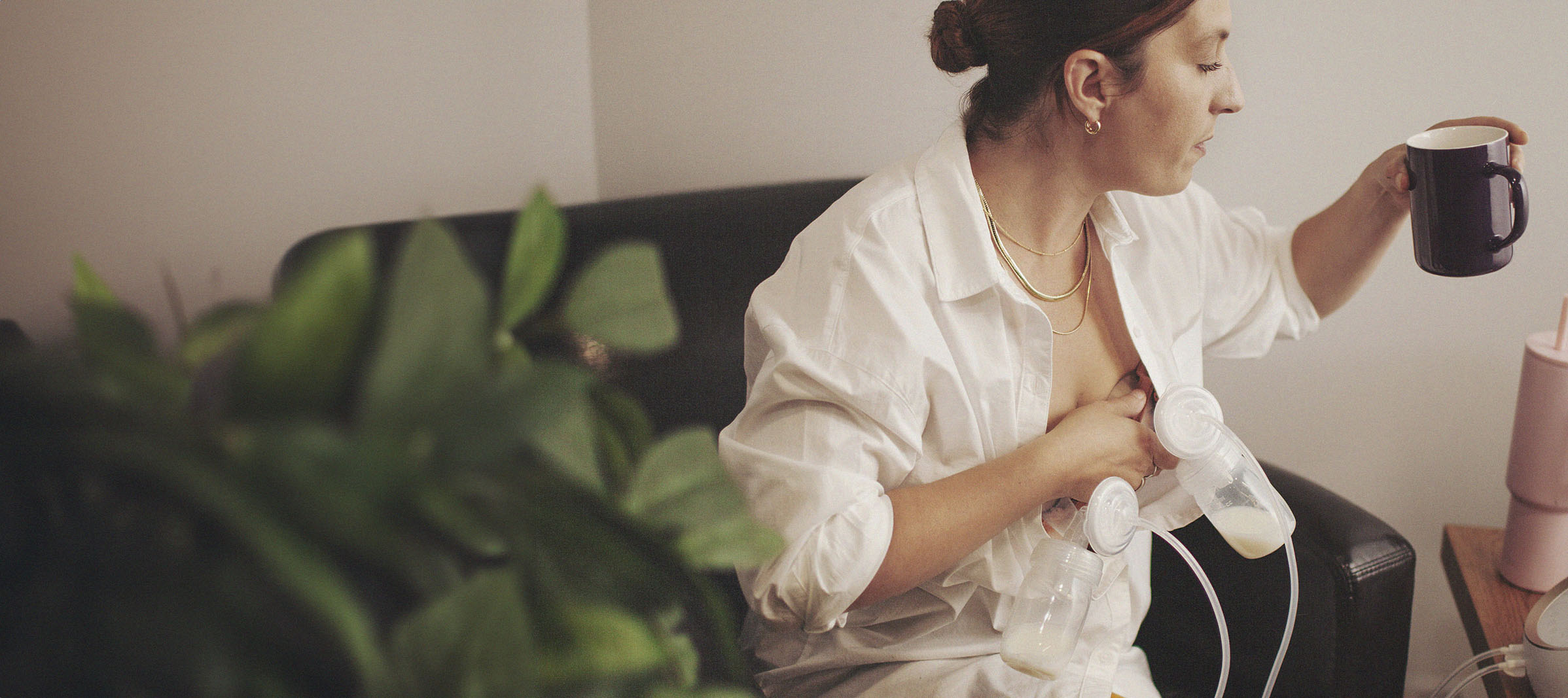 A smiling woman of European descent sits in a comfortable chair and nurses her infant while speaking with a woman of African descent.